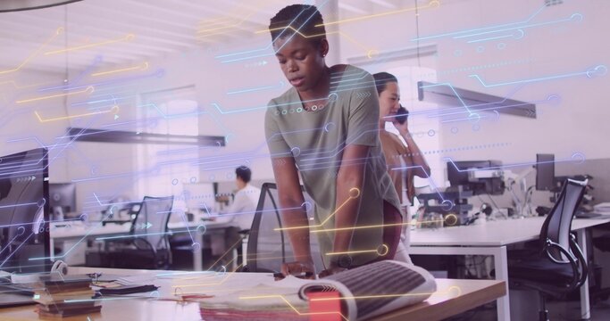 Leaning African American woman studying blueprint in open-plan office, with circuit overlay
