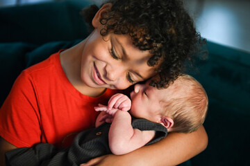 Smiling child snuggles newborn baby lovingly on dark couch