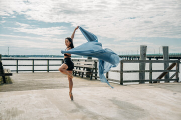 Ballerina dancing en pointe holding flowing fabric on pier
