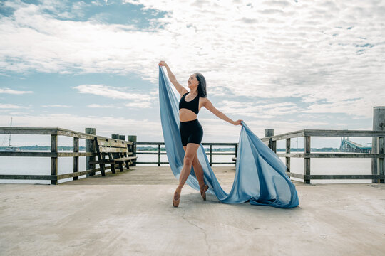 Ballerina dancing pointe shoes on pier with fabric