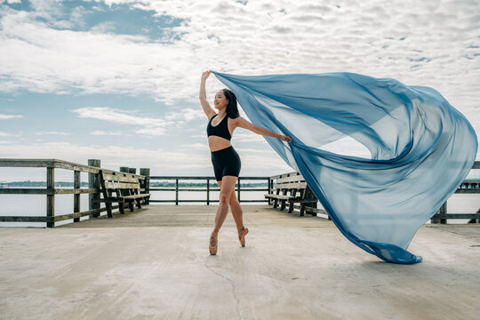 Ballet dancer twirls on pier with large flowing blue fabric