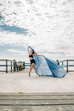 Ballerina dancing gracefully with blue fabric on pier