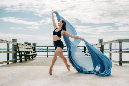 Ballerina dancing with flowing fabric on lake pier