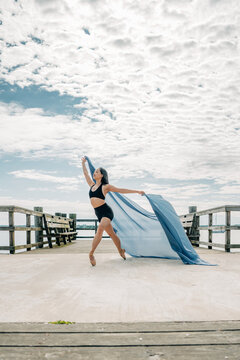Female ballet dancer performing with fabric on pier outdoors