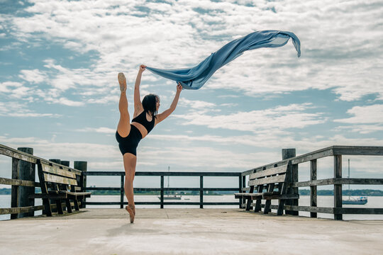 Ballerina on pier performing arabesque with flowing fabric