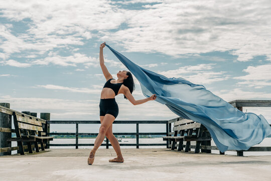 Ballerina dancing with floating fabric on pier under sky
