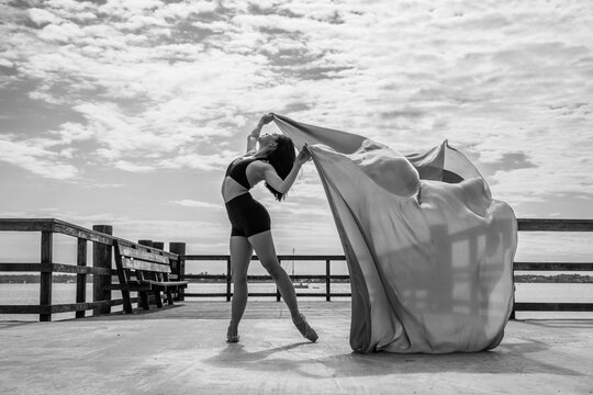 Graceful ballerina dancing with flowing fabric on pier