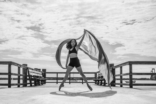 Female dancer posing on pier with flowing fabric