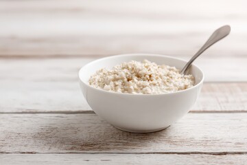 Minimalist breakfast with oatmeal in white bowl and spoon on light wooden background with shallow depth of field