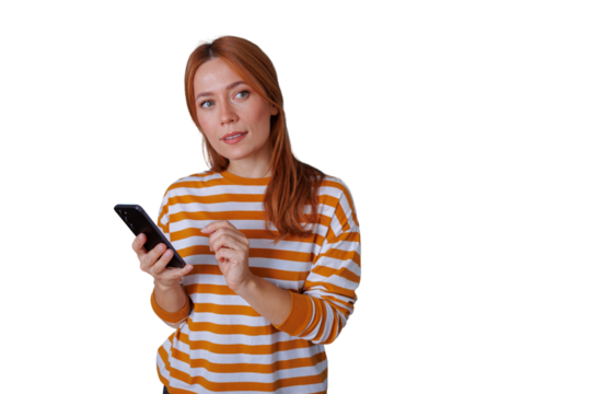 Young woman with red hair holding a smartphone, touching screen, and looking thoughtfully away. Transparent background included