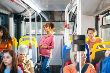 Pregnant woman commuting on a city bus, gently touching her belly while standing among other...
