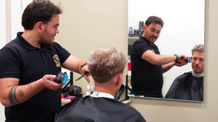 Focused barber smiles with client while cutting hair seen through mirror