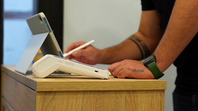 Close up of customer paying with phone on dataphone as barber takes notes on tablet