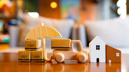 Wooden toy truck, cardboard boxes, umbrella and house model symbolizing logistics, delivery service, cargo insurance and e-commerce safety on wooden table with cozy home background.