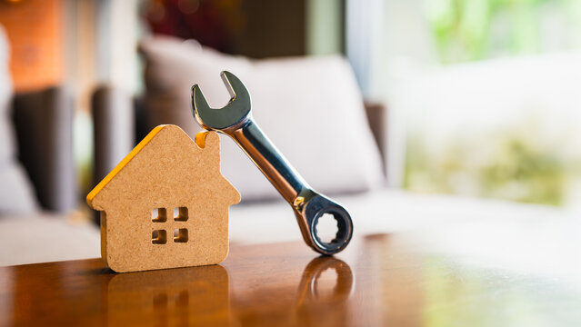 Wooden house model with metal wrench on wooden table, symbolizing home maintenance, repair service, real estate improvement, construction, and DIY renovation in domestic setting.