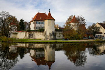 Obraz premium Blutenburg Castle in Munich, Germany, reflecting in the serene water, with people enjoying the autumn day along the shore
