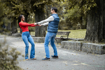 A joyful couple engages in a playful moment in a scenic park, showcasing love and connection as they hold hands and dance amidst nature's beauty during their leisure time.