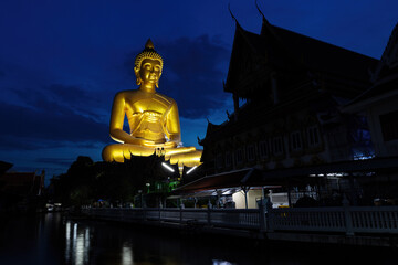 Giant golden Budda statue towering 69 meters (226 feet) over the Buddhist temple of Wat Paknam in Bangkok, Thailand. Backlit with the deep blue twilight sky.

