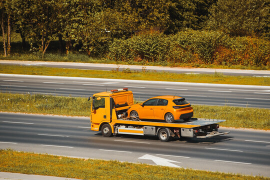 Yellow car towed by flatbed truck on highway