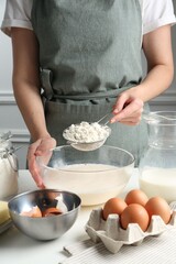 Making batter (liquid dough). Woman sieving flour into bowl at white table indoors, closeup
