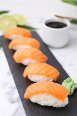 Delicious nigiri sushi with salmon, wasabi and soy sauce on white marble table, closeup