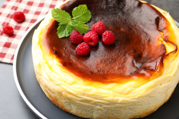 Tasty Basque cheesecake with raspberries and mint on grey textured table, closeup