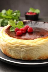Tasty Basque cheesecake with raspberries and mint on grey textured table, closeup