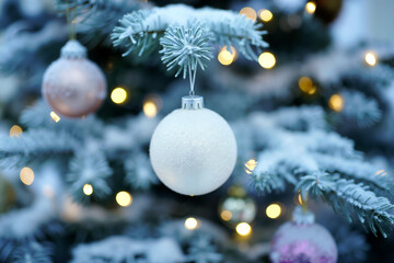 Close-up of frosted Christmas tree branch with white ball ornament and warm golden lights creating festive bokeh background. Generative AI.
