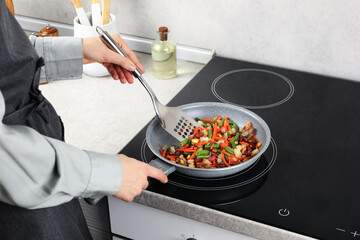 Woman stirring mix of fresh vegetables with slotted spatula in frying pan, closeup