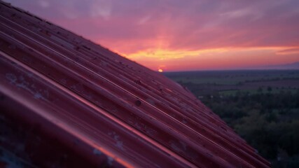 As sun sinking below horizon, camera panning down rusted roof panel on rural rooftop, with farmland - Powered by Adobe