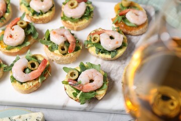 Delicious bruschettas with shrimps and wine on light table, selective focus