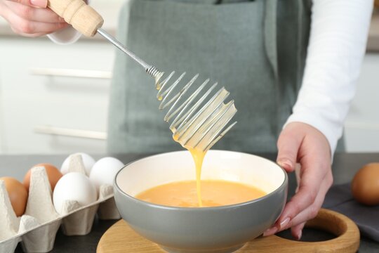 Woman beating eggs with whisk at grey table in kitchen, closeup
