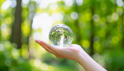 森のなかで手にのせた透明なガラス球のアップ