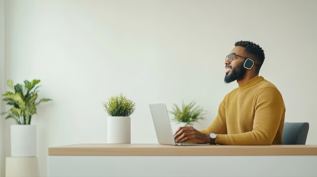 Professional african man in yellow sweater with glasses and headphones intently works on laptop at modern office desk, representing remote work and effective communication solutions. - Powered by Adobe