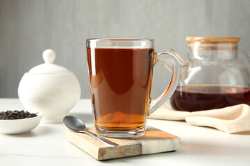 Tasty tea in glass cup and teaspoon on white table against grey background, closeup