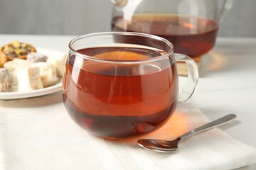 Tasty tea in glass cup and teaspoon on white table against grey background, closeup