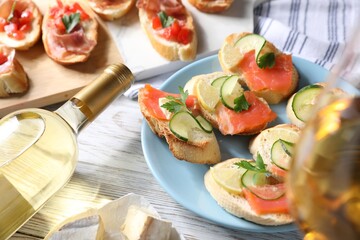 Tasty bruschettas with salmon, cucumber, lemon, prosciutto and wine on white wooden table, closeup