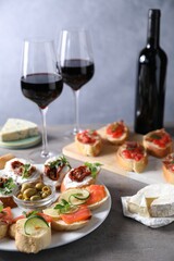 Different tasty bruschettas and red wine on grey textured table, closeup