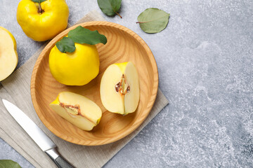 Ripe quinces, green leaves and knife on grey table, flat lay. Space for text