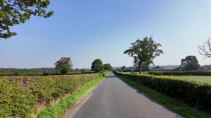 Slow motion footage driving and traveling down a country road in North Yorkshire in the UK showing British farmers fields on either side of the country lane on a sunny day in the summer time