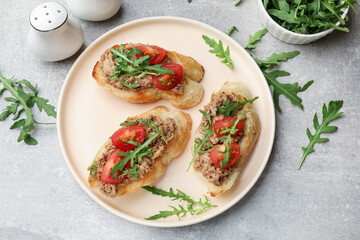 Delicious bruschettas with tuna, tomatoes and arugula on grey table, flat lay
