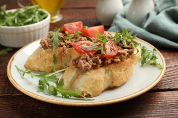 Delicious bruschettas with tuna, tomatoes and arugula on wooden table, closeup