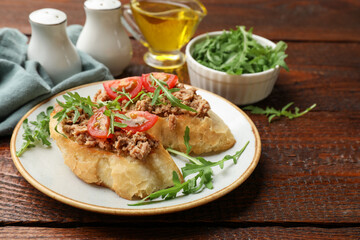 Delicious bruschettas with tuna, tomatoes and arugula on wooden table, closeup