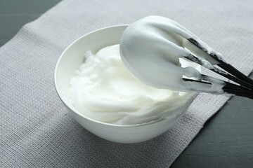 Whipped whites in bowl, whisk and eggs on grey wooden table, closeup