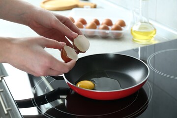 Woman cracking egg into frying pan in kitchen, closeup