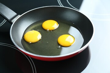 Frying pan with raw chicken eggs on cooktop in kitchen, closeup