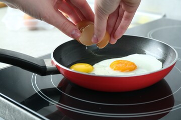 Woman cracking egg into frying pan in kitchen, closeup