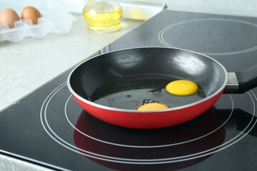 Frying pan with raw chicken eggs on cooktop in kitchen, closeup