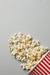 Vertical view of delicious popcorn in a striped cardboard bucket on a grey background