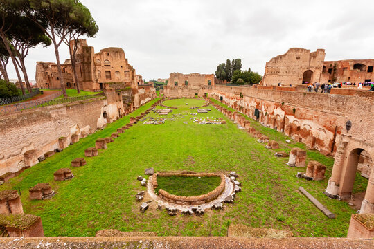 Rome, Italy - 04 November 2012: View of the vibrant green field nestled within the ancient ruins of the Palatine Hill, framed by weathered brick and stone under a muted sky.